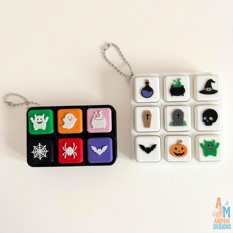 May include: Two rectangular silicone cases with attached ball chains. The black case features six colorful squares with white Halloween icons: a monster, ghost, cauldron, spiderweb, spider, and bat. The white case has nine white squares with icons.