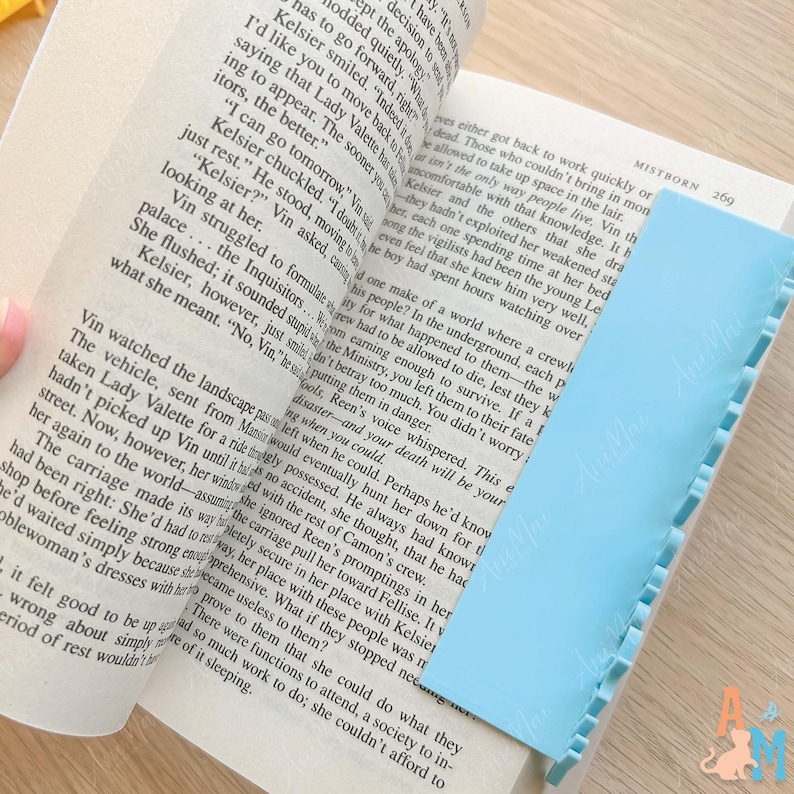 K&ouml;nnte beinhalten: Ein hellblaues Lesezeichen mit gewelltem Rand liegt auf den Seiten eines ge&ouml;ffneten Buches. Das Buch ist aufgeschlagen und zeigt gedruckten Text. Das Lesezeichen ist rechteckig und aus flexiblem Material.