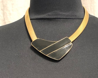 May include: A gold chain necklace with a black geometric pendant. The pendant has a shiny, enamel-like finish.