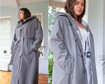 May include: A gray hooded trench coat with a fur-lined collar and a belt. The coat has a button closure and pockets.