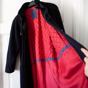 May include: A black long coat with a red quilted lining. The coat has a hood and a green velvet collar.