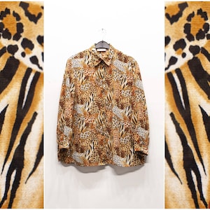 May include: A button-down shirt with a brown and tan animal print, including leopard spots and zebra stripes. The long-sleeved shirt is hanging on a hanger against a white background. The shirt's pattern is repeated on the sides of the image.