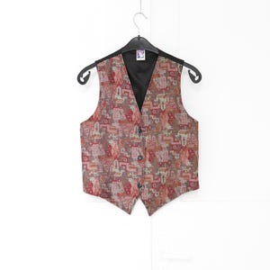 May include: A sleeveless vest featuring a multi-colored geometric and abstract pattern in shades of red, brown, and beige. The garment has a V-neckline, a black interior lining, and three dark buttons down the front center, all displayed on a black hanger.