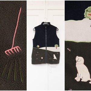 Può includere: Un gilet in pile blu navy con cerniera a tutta lunghezza. Il gilet presenta disegni ricamati di un cane, alberi e un rastrello. La parte inferiore è marrone scuro e la parte superiore è blu navy.
