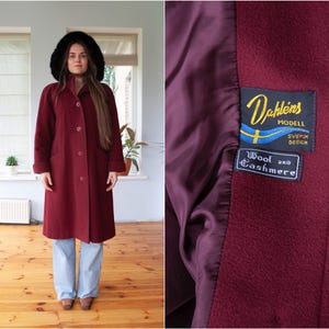 May include: A long, burgundy wool and cashmere coat with a fur collar. The coat has a label that reads "Dahléns Modell Svensk Design Wool and Cashmere".