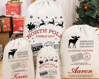 May include: A collection of cream-colored Christmas gift sacks with drawstring closures. Each sack features a black graphic of a reindeer-pulled sleigh or a moose, along with the words "North Pole" and "Overnight Delivery". Names are printed on some sacks.