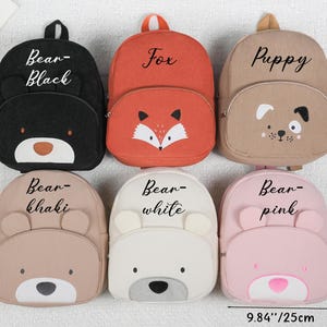 May include: Six corduroy backpacks in various colors, each with an animal face design. The backpacks include a black bear, orange fox, tan puppy, khaki bear, white bear, and pink bear. The backpacks are approximately 9.84 inches wide and 11.8 inches tall.