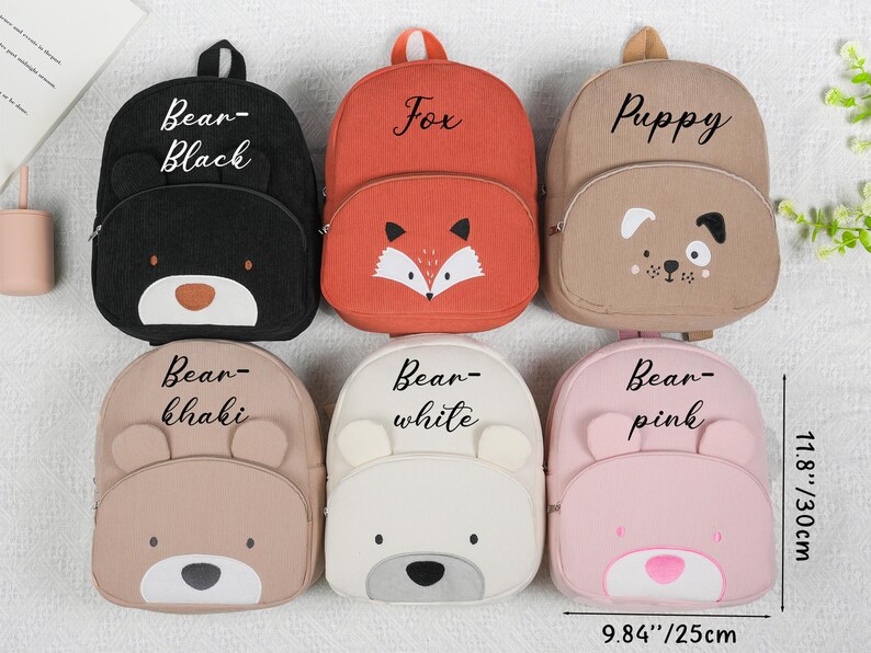 May include: Six corduroy backpacks in various colors, each with an animal face design. The backpacks include a black bear, orange fox, tan puppy, khaki bear, white bear, and pink bear. The backpacks are approximately 9.84 inches wide and 11.8 inches tall.