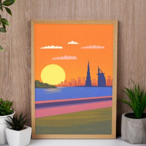 May include: A framed art print depicting a sunset over a city skyline. The artwork features an orange sky, a yellow sun, and silhouettes of buildings, including a tall tower and a sail-shaped structure. The foreground shows water and a pathway.