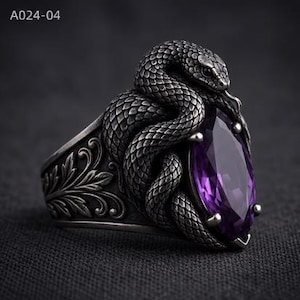 Könnte beinhalten: Ein silberner Ring mit einer gewundenen Schlange mit detaillierten Schuppen und herausgestreckter Zunge, besetzt mit einem großen, oval geschliffenen violetten Edelstein. Die Ringschiene zeigt filigrane Blattgravuren. Der Text A024-04 ist sichtbar.
