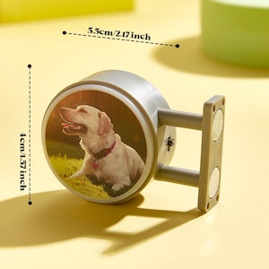 Könnte beinhalten: Ein grauer magnetischer Wandhaken mit einem kreisförmigen Design, das ein Foto eines goldenen Labradors zeigt. Der Haken ist 5,5 cm breit und 4 cm hoch. Der Hund trägt ein rosa Halsband und liegt auf Gras.