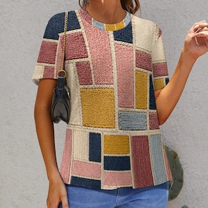 Peut inclure: T-shirt à manches courtes avec un motif patchwork. Le t-shirt présente une variété de formes rectangulaires et carrées dans des tons de rose, jaune, bleu et crème. Le design donne l'apparence d'une texture tricotée ou tissée.