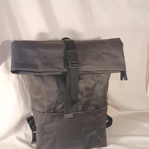 May include: A dark gray roll-top backpack with a black buckle closure and adjustable straps. The backpack has a large main compartment and a front pocket. The material appears to be a durable, water-resistant fabric.