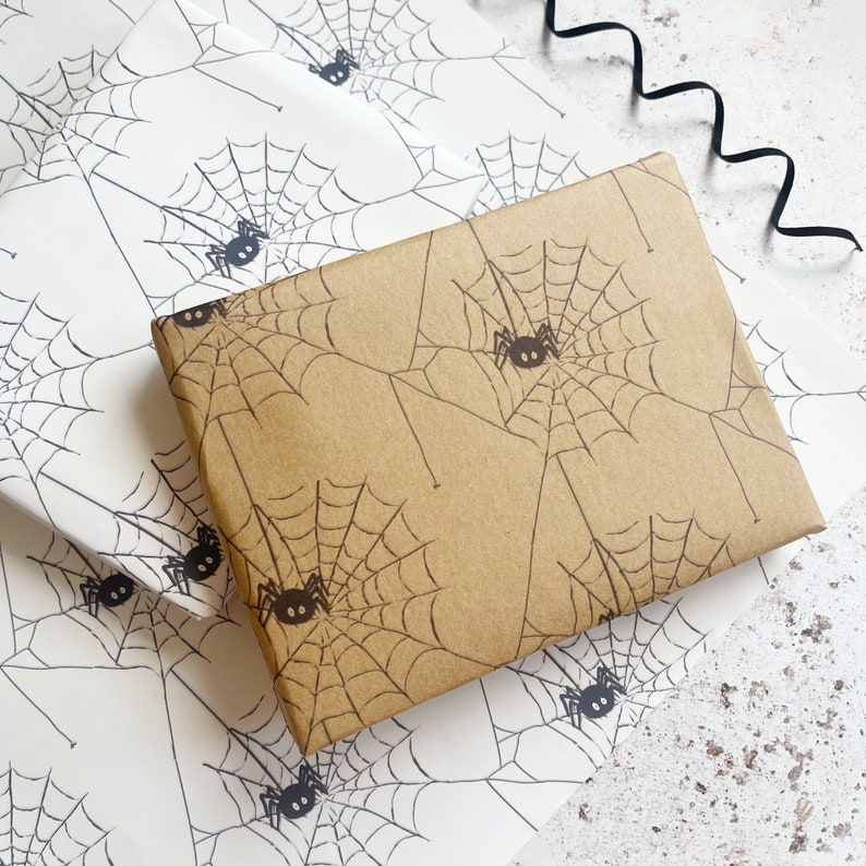 Pu&ograve; includere: Due fogli di carta da regalo con un motivo a ragnatela e ragno. Un foglio &egrave; bianco con ragni neri e l'altro &egrave; marrone con ragni neri.