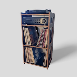 Peut inclure: Meuble de rangement en bois pour disques vinyles avec cadre et étagères noirs. L'unité contient des disques vinyles et du matériel audio, dont une platine et un récepteur. Les disques sont visibles sur les étagères.