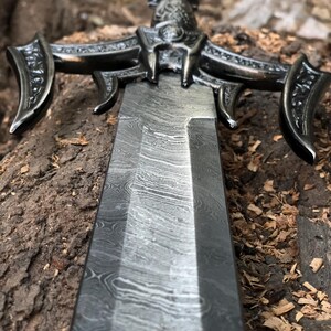 May include: A close-up of a sword with an intricate, ornate handle and a blade with a distinctive, wavy pattern.