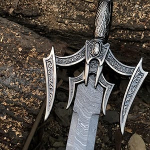 May include: A silver sword with a decorative handle and a patterned blade. The sword has a decorative guard with intricate designs.