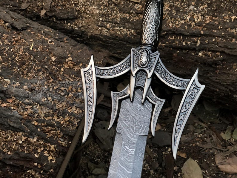 May include: A silver sword with a decorative handle and a patterned blade. The sword has a decorative guard with intricate designs.