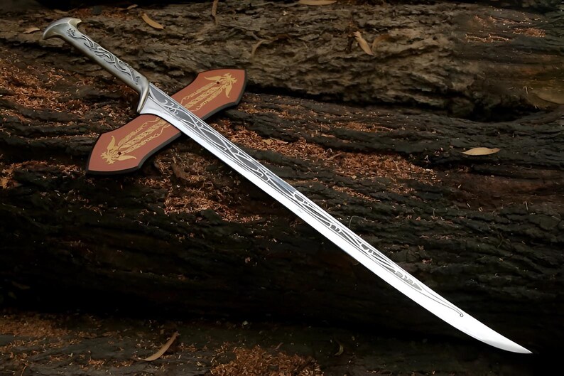 May include: A silver sword with a decorative handle and a wooden scabbard. The sword has a detailed design on the blade and is resting on a wooden surface.