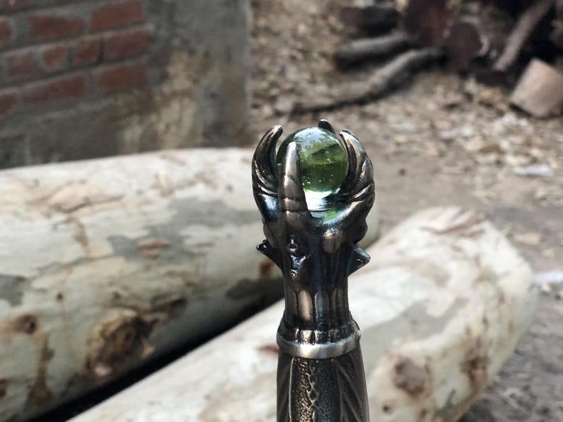 May include: Close-up of a sword hilt featuring an intricate dragon design. The hilt is topped with a green glass orb.
