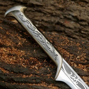 May include: A silver sword with a detailed, intricate design on the handle and blade. The handle is decorated with a floral pattern.