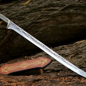 May include: A silver sword with a decorative handle and blade. The sword is resting on a brown wooden surface with a decorative stand.
