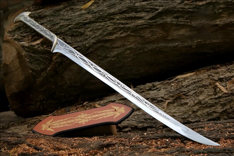 May include: A silver sword with a decorative handle and blade. The sword is resting on a brown wooden surface with a decorative stand.