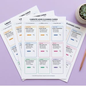 May include: A set of white 5-Minute ADHD Cleaning Cards printed with black text and colorful dashed borders. The cards feature household cleaning tasks organized by room, including kitchen, living room, bedroom, and bathroom zones with checkboxes.
