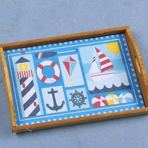 May include: A rectangular wooden tray with a nautical theme. The tray's interior features a blue background with illustrations of a lighthouse, sailboat, anchor, and life preserver. The tray has a light brown wooden frame.