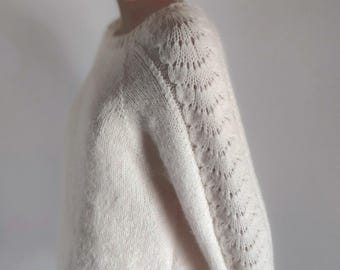 Può includere: Un maglione di lana color crema con un delicato motivo a pizzo sulle maniche.