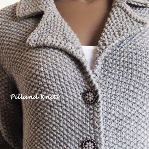 May include: A close-up of a gray knitted cardigan with a collar and two buttons. The cardigan has a textured knit pattern and the buttons have a floral design.