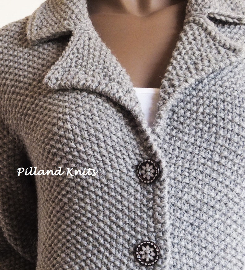 May include: A close-up of a gray knitted cardigan with a collar and two buttons. The cardigan has a textured knit pattern and the buttons have a floral design.
