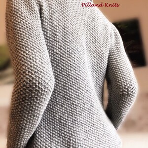 May include: A gray knitted cardigan with a textured stitch pattern. The cardigan has a collar and long sleeves. The text "Pilland Knits" is visible on the back of the cardigan.