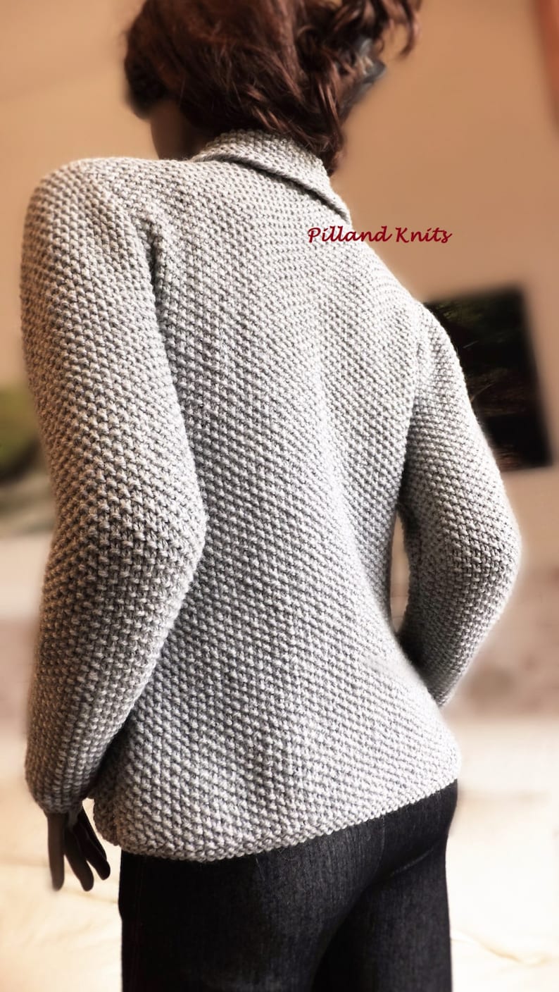 May include: A gray knitted cardigan with a textured stitch pattern. The cardigan has a collar and long sleeves. The text "Pilland Knits" is visible on the back of the cardigan.