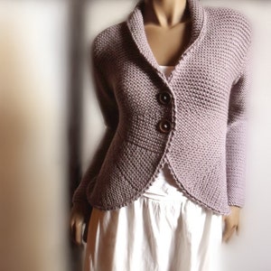 Könnte beinhalten: Ein mauvefarbener Strickcardigan mit Schalkragen und zwei Knöpfen. Der Cardigan hat eine figurbetonte Silhouette und einen leicht abgerundeten Saum.