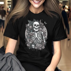 以下が含まれることがあります： 花、カボチャ、蝶に囲まれた、詳細なスケルトンデザインが特徴の黒いTシャツ。スケルトンは中心的な焦点であり、複雑な骨のディテールがあります。デザインは灰色の円形の背景に設定されています。