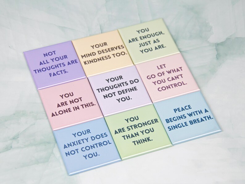 May include: Nine colourful square tiles with inspirational quotes printed on them. The quotes include "Not all your thoughts are facts", "Your mind deserves kindness too", "You are enough, just as you are", "You are not alone in this", "Your thoughts do not define you", "Let go of what you can't control", "Your anxiety does not control you", "You are stronger than you think", and "Peace begins with a single breath".
