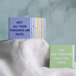 May include: A set of square magnets in pastel colors featuring printed text. One purple magnet displays the text NOT ALL YOUR THOUGHTS ARE FACTS. A separate light green magnet displays the text YOU ARE STRONGER THAN YOU THINK in white lettering.