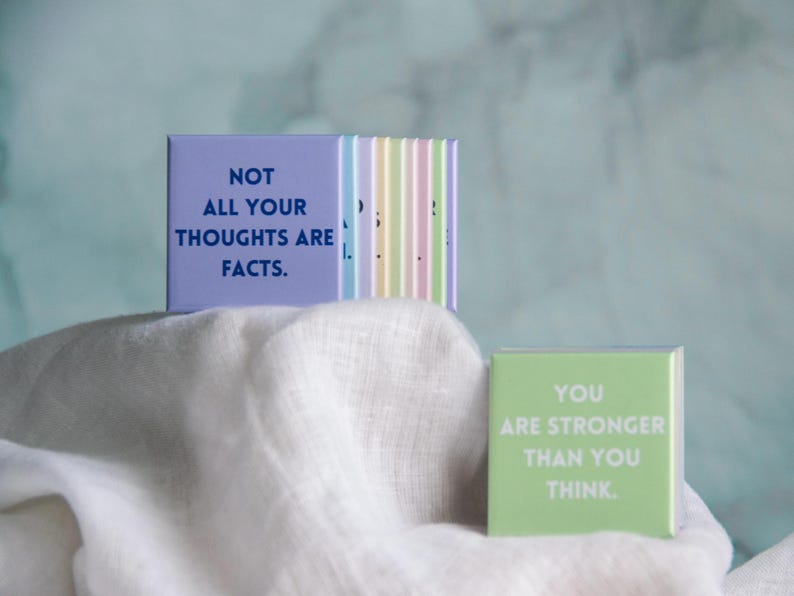 May include: A set of square magnets in pastel colors featuring printed text. One purple magnet displays the text NOT ALL YOUR THOUGHTS ARE FACTS. A separate light green magnet displays the text YOU ARE STRONGER THAN YOU THINK in white lettering.