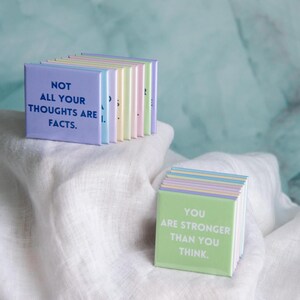 May include: A collection of square magnets in pastel colors. One stack features the text NOT ALL YOUR THOUGHTS ARE FACTS in dark blue. Another stack displays the text YOU ARE STRONGER THAN YOU THINK in white on a light green background.