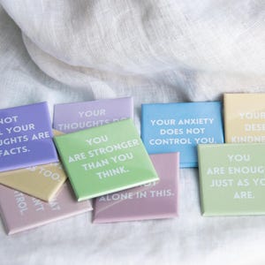 May include: A collection of square magnets in pastel colors, each featuring white text with affirmations including Not all your thoughts are facts, You are stronger than you think, Your anxiety does not control you, Your mind deserves kindness too, and You are enough, just as you are.