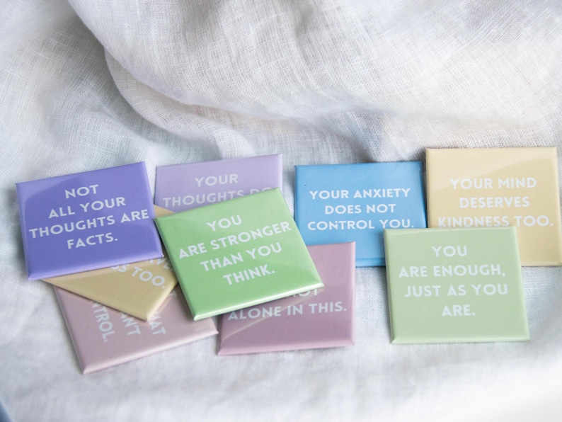 May include: A collection of square magnets in pastel colors, each featuring white text with affirmations including Not all your thoughts are facts, You are stronger than you think, Your anxiety does not control you, Your mind deserves kindness too, and You are enough, just as you are.