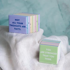 May include: A collection of square magnets in pastel colors, featuring printed text. One magnet displays the phrase NOT ALL YOUR THOUGHTS ARE FACTS in dark blue, while another shows YOU ARE STRONGER THAN YOU THINK in white text on green.