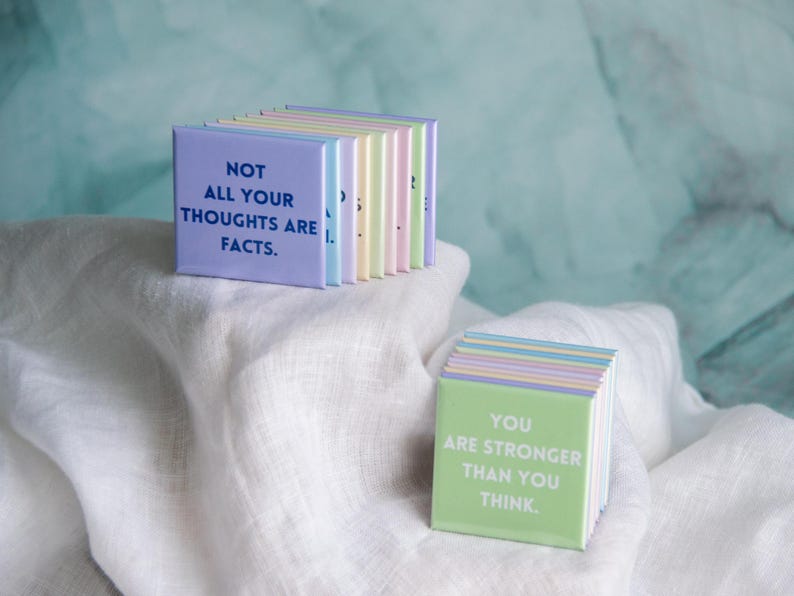 May include: A collection of square magnets in pastel colors, featuring printed text. One magnet displays the phrase NOT ALL YOUR THOUGHTS ARE FACTS in dark blue, while another shows YOU ARE STRONGER THAN YOU THINK in white text on green.