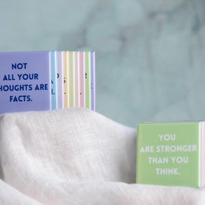 May include: A set of square magnets in pastel colors featuring motivational text. One lavender magnet displays the dark blue text NOT ALL YOUR THOUGHTS ARE FACTS. A light green magnet shows the white text YOU ARE STRONGER THAN YOU THINK.