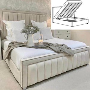 May include: A white upholstered bed frame with a tufted headboard and a storage compartment underneath. The bed is made with a white duvet and pillows. A small tray with a pitcher and candle sits on the bed.