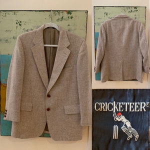 May include: A beige blazer with brown buttons and a Cricketteer logo on the inside pocket. The logo features a stick figure playing cricket.