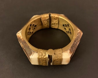 May include: A hexagonal brass bangle with a hinged opening. The bangle is decorated with intricate floral patterns and has a white bone inlay.