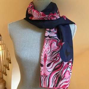 May include: A navy blue and pink silk scarf with a swirling abstract design. The scarf has the word "Sally" printed on the bottom right corner.
