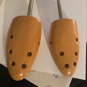 May include: A pair of wooden shoe trees with metal spring mechanisms. The shoe trees are light brown and have multiple holes.